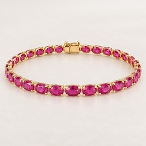 Könnte beinhalten: Ein goldenes Tennisarmband mit einer durchgehenden Reihe oval geschliffener, leuchtend pinker Edelsteine, die in polierte Goldfassungen eingefasst sind. Das Armband verfügt über einen sicheren Gold-Kastenschloss-Verschluss an den Enden.
