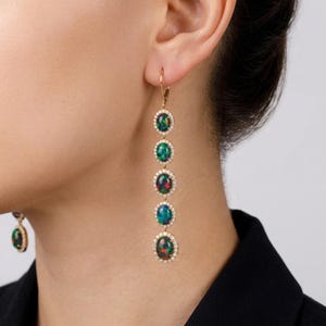 May include: A pair of long drop earrings featuring five oval-shaped dark opals arranged vertically. Each opal is surrounded by a halo of small white stones set in a gold-toned metal frame, suspended from a gold-toned lever back closure.