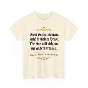 Könnte beinhalten: Ein cremefarbenes Kurzarm-T-Shirt mit schwarzem Text in gotischer Schrift: Zwei Seelen wohnen, ach! in meiner Brust, Die eine will sich von der andern trennen. Unter dem Text steht der Name Johann Wolfgang von Goethe in schwarzen Buchstaben.