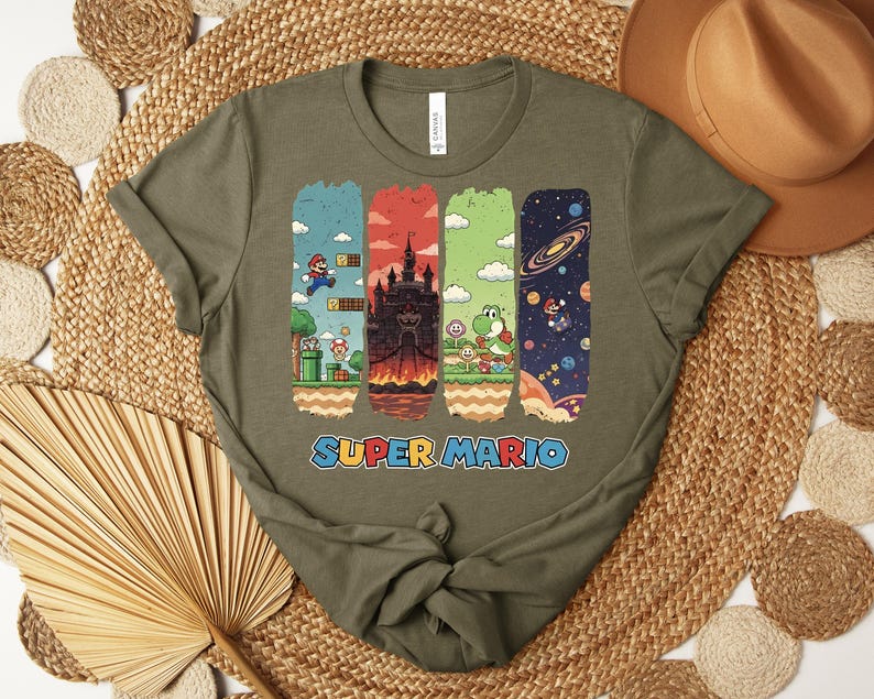 May include: Olive green t-shirt featuring a colorful Super Mario graphic. The design includes four vertical panels depicting scenes from the game, with the words "SUPER MARIO" in a blue and orange font.