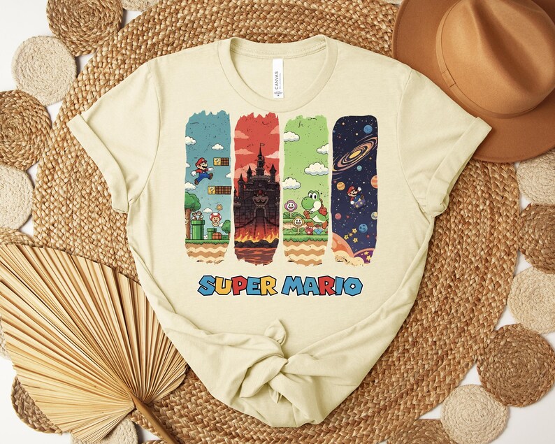 May include: Cream-colored t-shirt featuring a colorful Super Mario graphic. The design includes four vertical panels with scenes from the game, including Mario, a castle, Yoshi, and a space scene. The words "SUPER MARIO" are printed in blue.