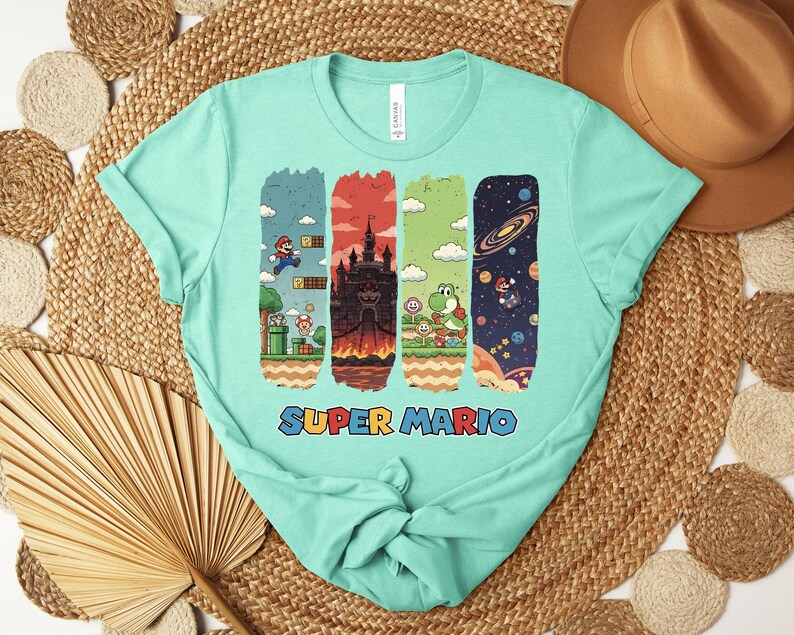 May include: A light teal t-shirt featuring a Super Mario graphic. The graphic includes four vertical panels with scenes from the game, including Mario, a castle, Yoshi, and space. The words "SUPER MARIO" are printed in colorful letters below the panels.