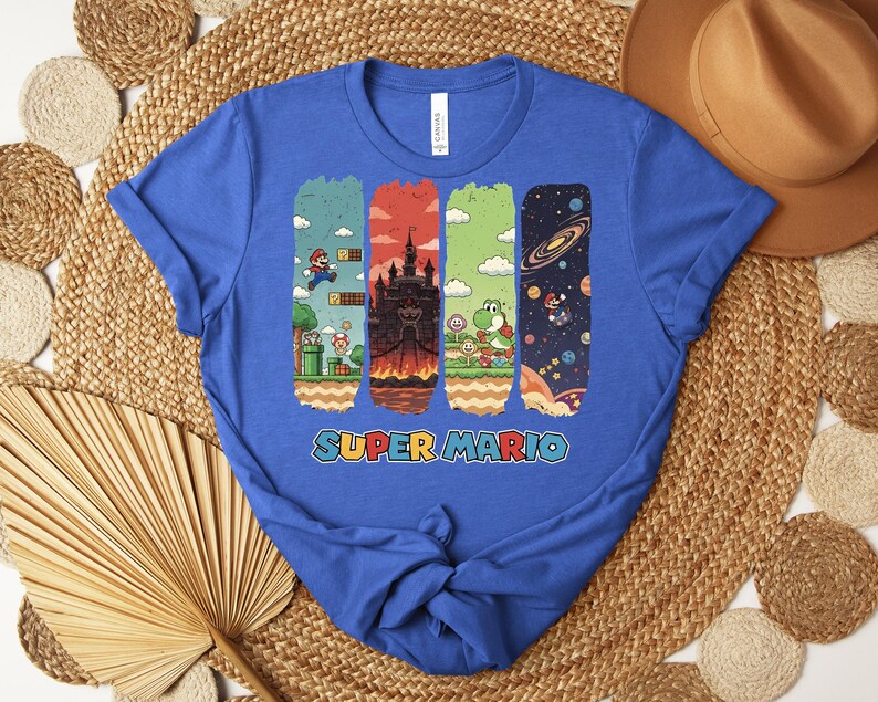 May include: A royal blue t-shirt featuring a colorful graphic of Super Mario characters and scenes. The design includes images of Mario, a castle, Yoshi, and a space scene. The words "SUPER MARIO" are printed in a colorful font.
