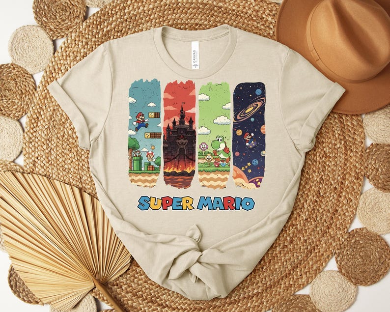 May include: Beige t-shirt featuring a Super Mario design. The graphic includes four vertical panels with scenes from the game, including Mario, a castle, Yoshi, and space. The words "SUPER MARIO" are printed in blue and red.