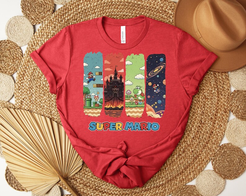 May include: A red t-shirt featuring a Super Mario design. The graphic includes four vertical rectangular panels with scenes from the game, including Mario, a castle, Yoshi, and a space scene. The words "SUPER MARIO" are printed in blue.