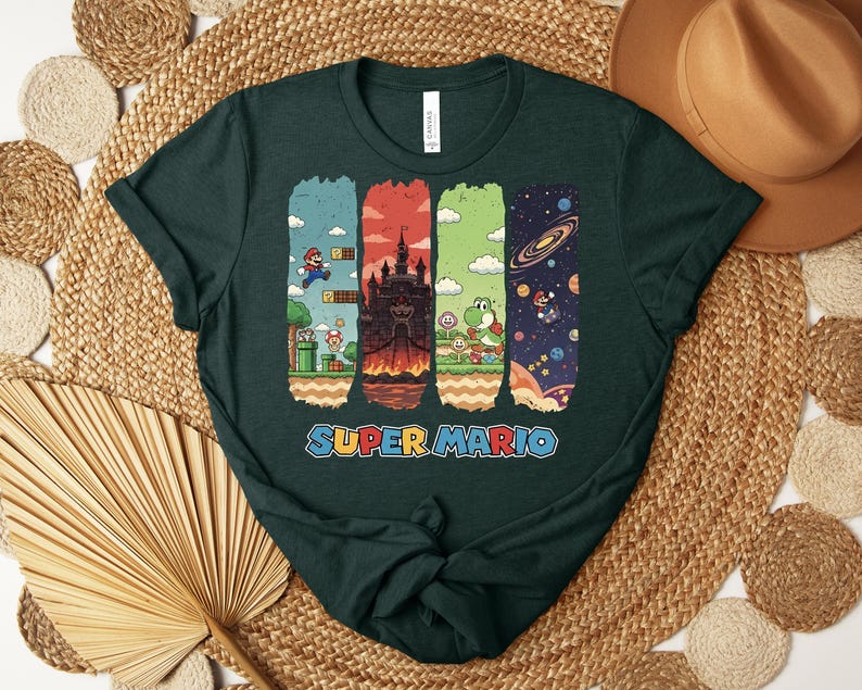May include: Dark green t-shirt featuring a colorful Super Mario graphic. The design includes scenes from the game, such as Mario jumping, a castle, Yoshi, and a space scene. The words "SUPER MARIO" are printed in blue and orange.