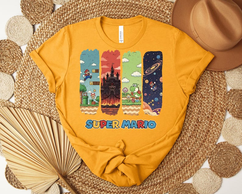 May include: Mustard yellow t-shirt featuring a Super Mario graphic. The graphic includes four vertical panels with scenes from the game, including Mario, a castle, Yoshi, and a space scene. The words "SUPER MARIO" are printed in blue.