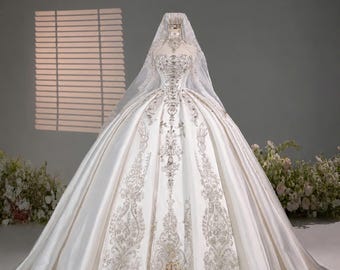May include: A white ball gown wedding dress featuring a strapless bodice and a full skirt adorned with intricate silver embroidery and crystal embellishments. A matching sheer veil covers the head and shoulders. The text TIỆM VÁY CƯỚI is visible.