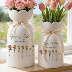 May include: Two white ceramic vases with scalloped tops, each tied with a beige ribbon. One vase holds pink roses, the other holds pink and yellow tulips. The text "Grandma's Garden" and "Gigi's Garden" are printed on the vases, along with the phrase "love grows here".