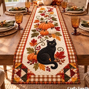 May include: A rectangular table runner featuring a quilted design with a central black cat, orange and white pumpkins, autumn leaves, and red berries. The border displays a plaid pattern in brown, orange, and red tones with geometric corner accents.
