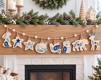 May include: A decorative garland featuring wooden ornaments shaped like a rabbit, stars, a fox, a bird, an owl, a bear, and a deer. Each ornament is painted with blue floral and heart patterns, suspended on a jute string with white wooden beads.