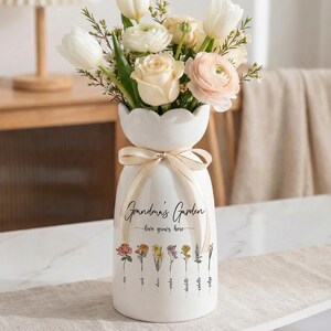 May include: A white ceramic vase with a floral arrangement of white tulips, roses, and pink flowers. The vase has a decorative bow and the text "Grandma's Garden - love grows here". Below the text are illustrations of various flowers.