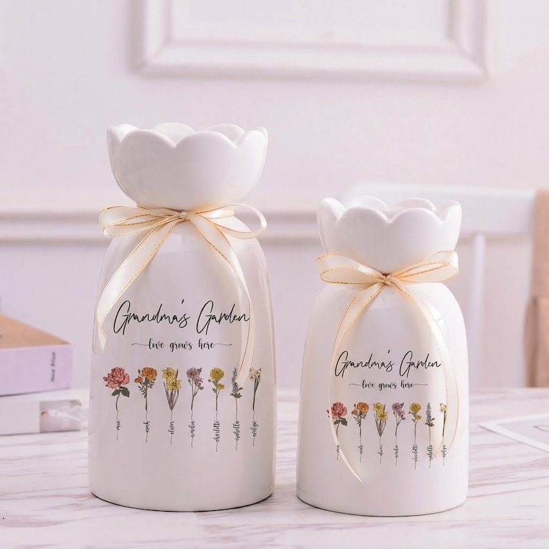 May include: Two white ceramic vases with a floral design and the text "Grandma's Garden". Each vase has a scalloped top and is tied with a cream-colored ribbon. The vases are decorated with various flowers.