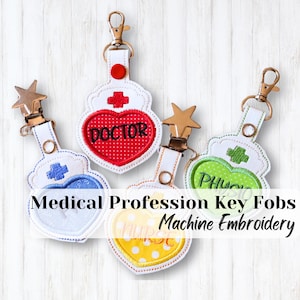 May include: Key fobs for medical professionals, featuring machine embroidery. Designs include a red heart with "DOCTOR", a blue heart, a green heart with "PHYS", and a yellow heart with "NURSE". Each fob has a metal clip.