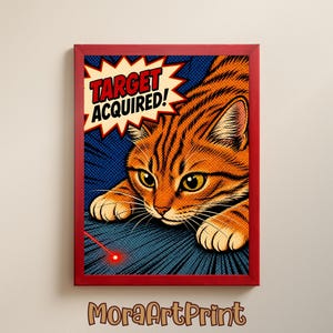 Op de afbeelding: Een ingelijste print met een stripboekachtige illustratie van een oranje tijgerkat met gele ogen. De kat is gefocust op een rode laserpointer. Tekst in een ster luidt "TARGET ACQUIRED!". De print zit in een rode lijst.