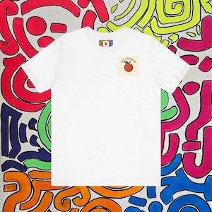 May include: White t-shirt with a small square graphic featuring a red apple and the text "LEE CHARLIE." The shirt has a crew neck and short sleeves. The background is a colorful abstract design with red, yellow, green, blue, and orange shapes.