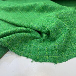 a close-up view of a green tweed fabric with a textured, woven appearance.