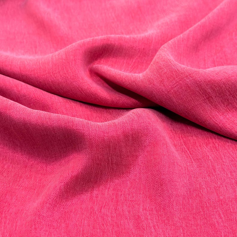 a close-up view of a bright pink fabric, with a slightly wrinkled texture.