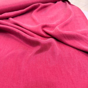 a close-up view of a vibrant pink fabric, possibly a piece of clothing or textile. The fabric appears to be wrinkled, giving it a soft and casual appearance.