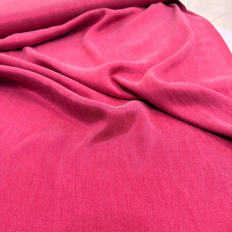 a close-up view of a vibrant pink fabric, possibly a piece of clothing or textile. The fabric appears to be wrinkled, giving it a soft and casual appearance.