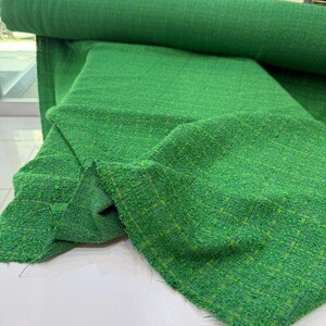 A roll of bright green tweed fabric is displayed on a white surface.