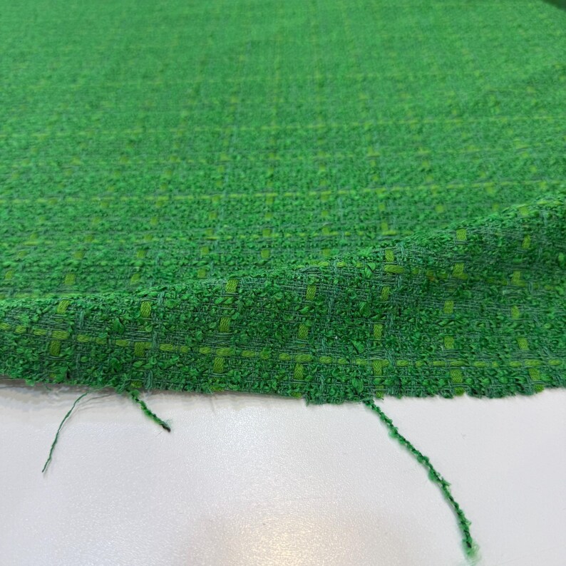 a close-up view of a green tweed fabric with a textured, woven appearance.