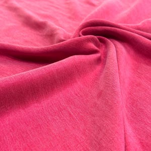 a close-up view of a vibrant pink fabric, with a slight curl and texture visible.