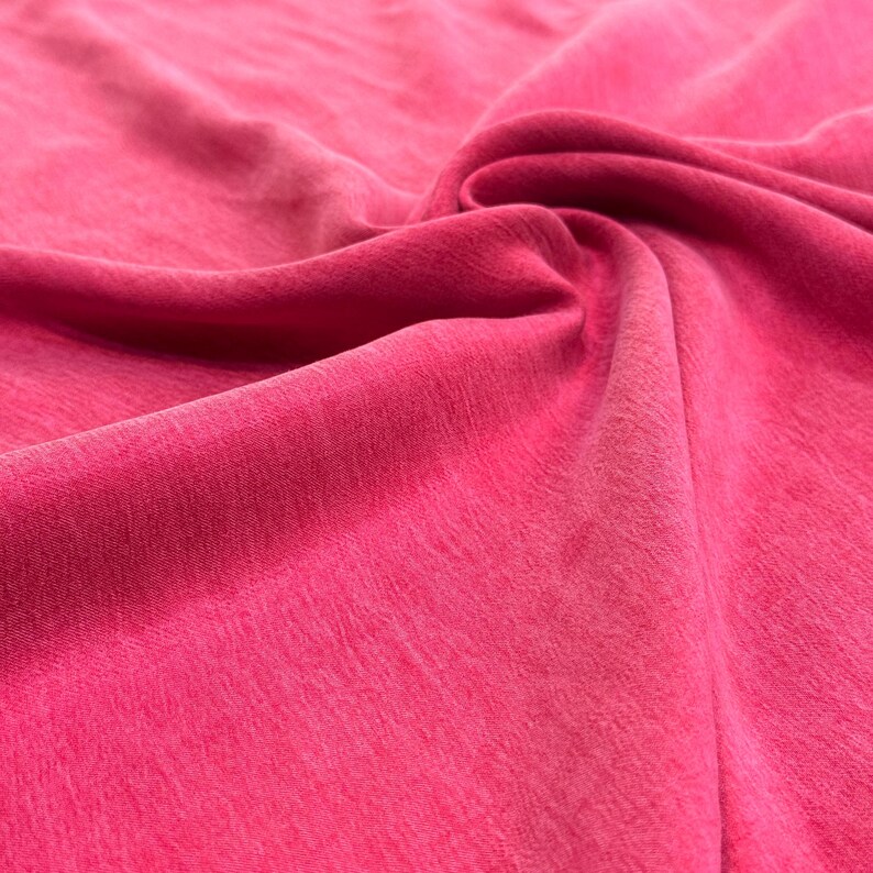 a close-up view of a vibrant pink fabric, with a slight curl and texture visible.