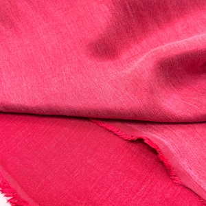 a close-up view of a vibrant red fabric, with a slightly curled and fringed edge. The fabric appears to be made of a soft, textured material, possibly cotton or a similar natural fiber. The image does not contain any other objects or text, and the focus is solely on the red fabric.