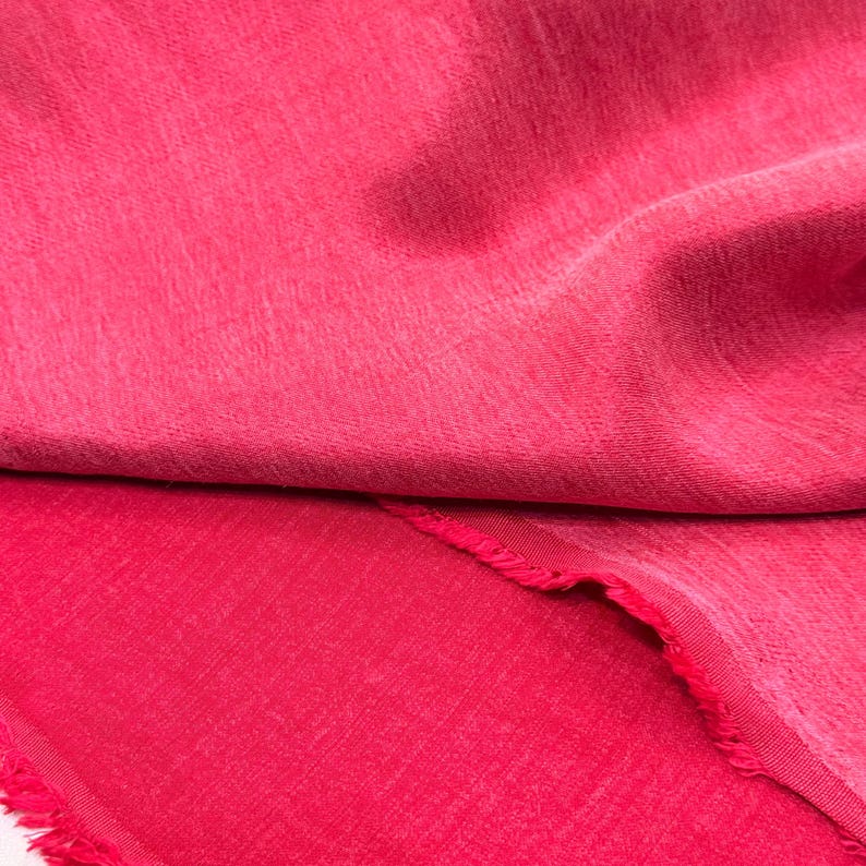 a close-up view of a vibrant red fabric, with a slightly curled and fringed edge. The fabric appears to be made of a soft, textured material, possibly cotton or a similar natural fiber. The image does not contain any other objects or text, and the focus is solely on the red fabric.