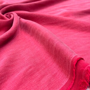 A close-up view of a vibrant red fabric, possibly cotton or silk, with a slightly wrinkled texture.