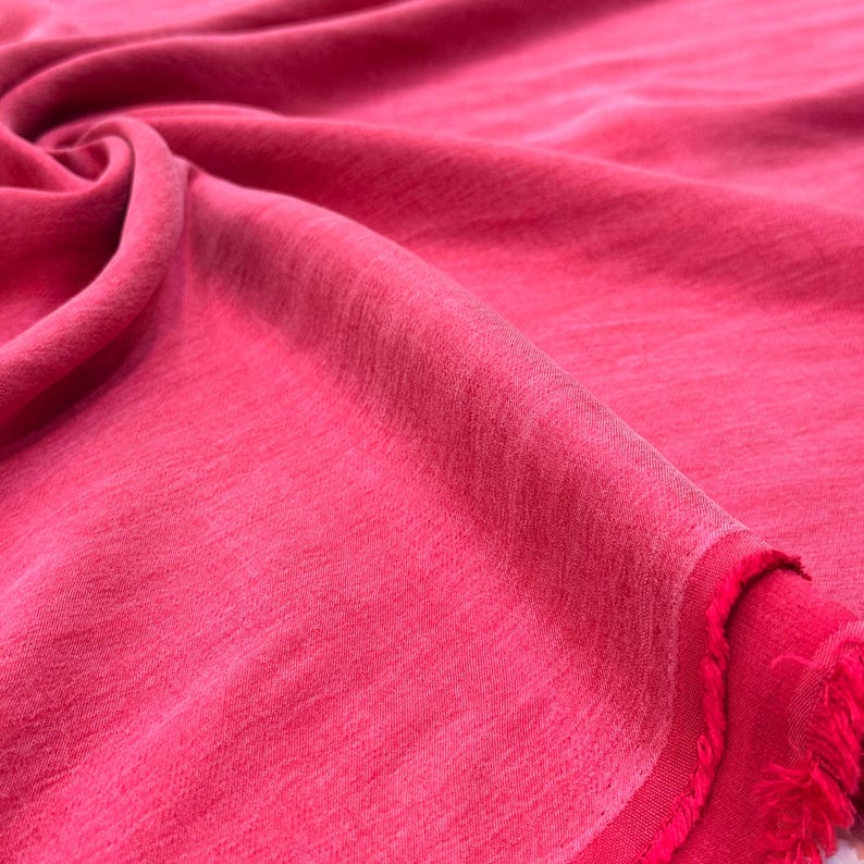 A close-up view of a vibrant red fabric, possibly cotton or silk, with a slightly wrinkled texture.