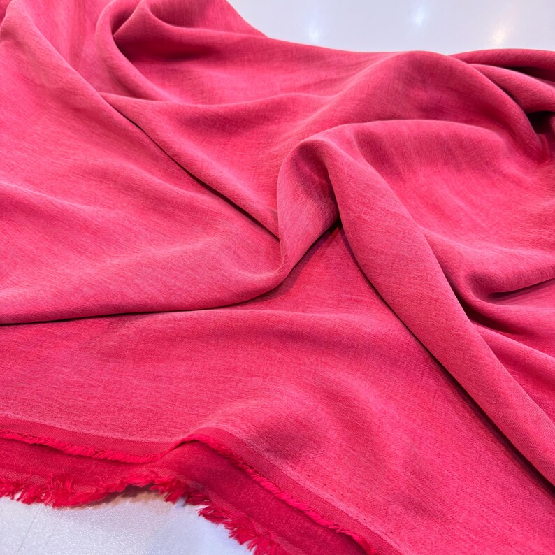 a close-up view of a vibrant red fabric, possibly a piece of clothing or a textile. The fabric appears to be soft and smooth, with a slightly wrinkled texture. The color of the fabric is quite bright and eye-catching, making it stand out in the image.