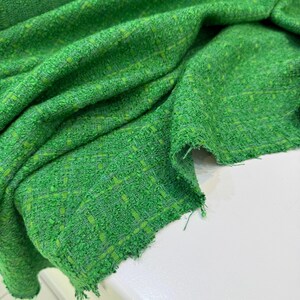 a close-up view of a green tweed fabric with a textured, woven appearance.