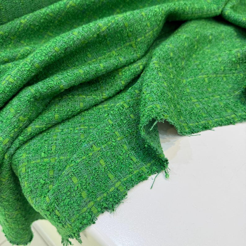 a close-up view of a green tweed fabric with a textured, woven appearance.
