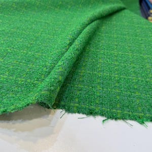 a close-up view of a green tweed fabric with a textured, woven appearance.