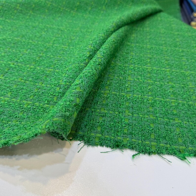 a close-up view of a green tweed fabric with a textured, woven appearance.