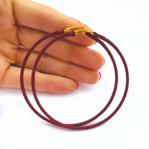 May include: A pair of burgundy hoop earrings with gold-toned clasps. The earrings are made of a soft, fabric-like material.