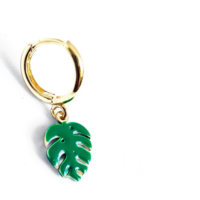 May include: Gold hoop earring with a green monstera leaf charm.