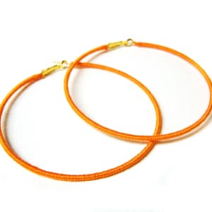 May include: A pair of orange hoop earrings with gold clasps.