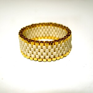 K&ouml;nnte beinhalten: Ein wei&szlig;er Perlenring mit goldener Einfassung. Der Ring besteht aus kleinen, quadratischen Perlen und hat ein schlichtes, elegantes Design.