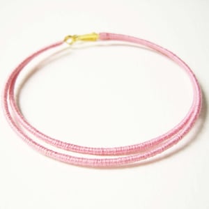 May include: A pink double-strand wire hoop necklace with a gold clasp.