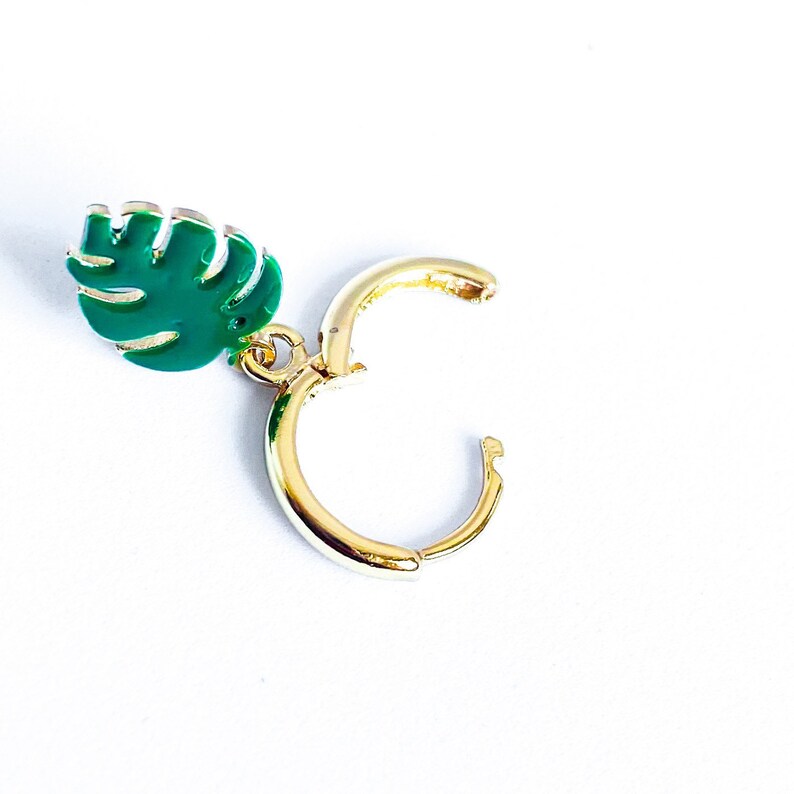 May include: Gold hoop earrings with a green leaf charm. The leaf charm is a tropical style.
