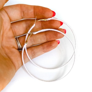 May include: A pair of white hoop earrings with a gold clasp. The earrings are made of a thin, woven material.