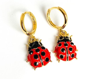 May include: A pair of gold hoop earrings with red and black ladybug charms. The ladybugs have black spots and are detailed with gold accents.