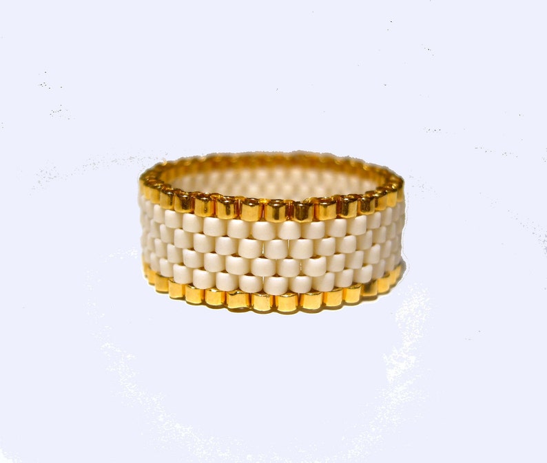 K&ouml;nnte beinhalten: Ein wei&szlig;er Perlenring mit einem goldenen Band oben und unten.