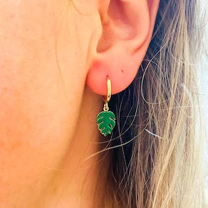 May include: Gold hoop earrings with a green monstera leaf charm hanging from each hoop.
