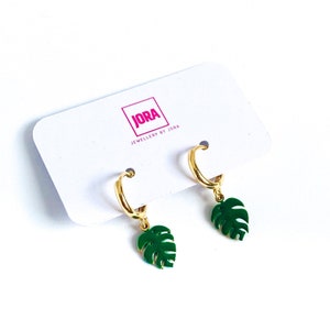May include: Gold hoop earrings with green monstera leaf charms. The earrings are displayed on a white card with the text "JORA JEWELLERY BY JORA".