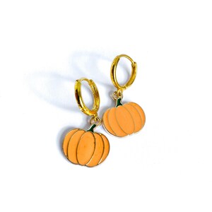 May include: A pair of gold hoop earrings with a peach-coloured pumpkin charm hanging from each hoop.