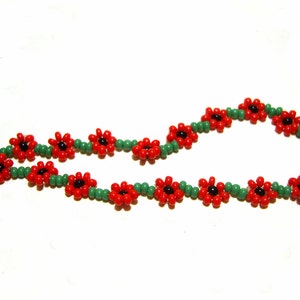 May include: A beaded bracelet with red flower-shaped beads and green spacer beads. The bracelet has a silver clasp.